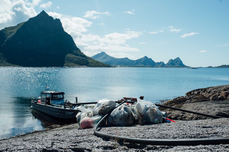 Collected waste bags on the rocks next to a workboat in the fjord