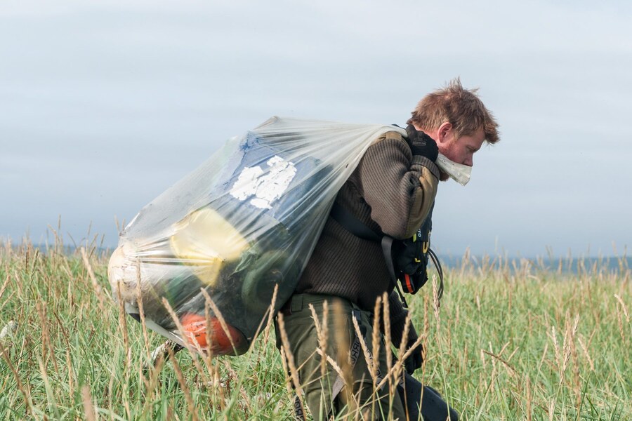 Volunteer carrying a bag of waste through coastal grass